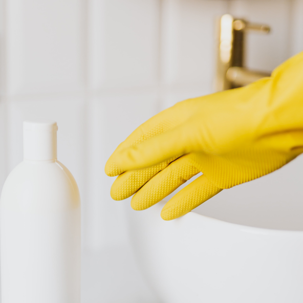 Une personne s'apprête à laver le robinet avec un gant et un produit d'entretien